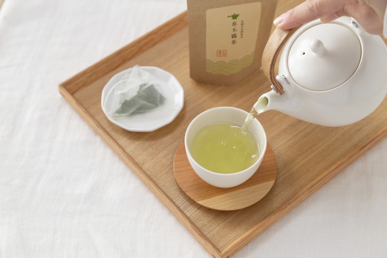 京玉露のオリジナルパッケージを背景に、急須から湯呑みへお茶を注ぐ様子